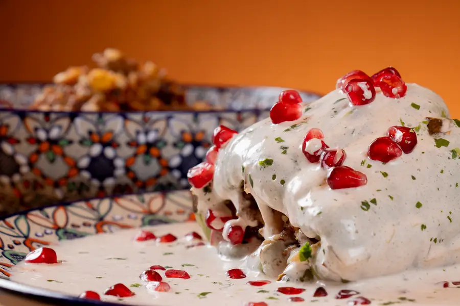 Gefüllte Paprika in heller Walnusssauce mit Granatapfelkernen auf bemaltem Keramikteller